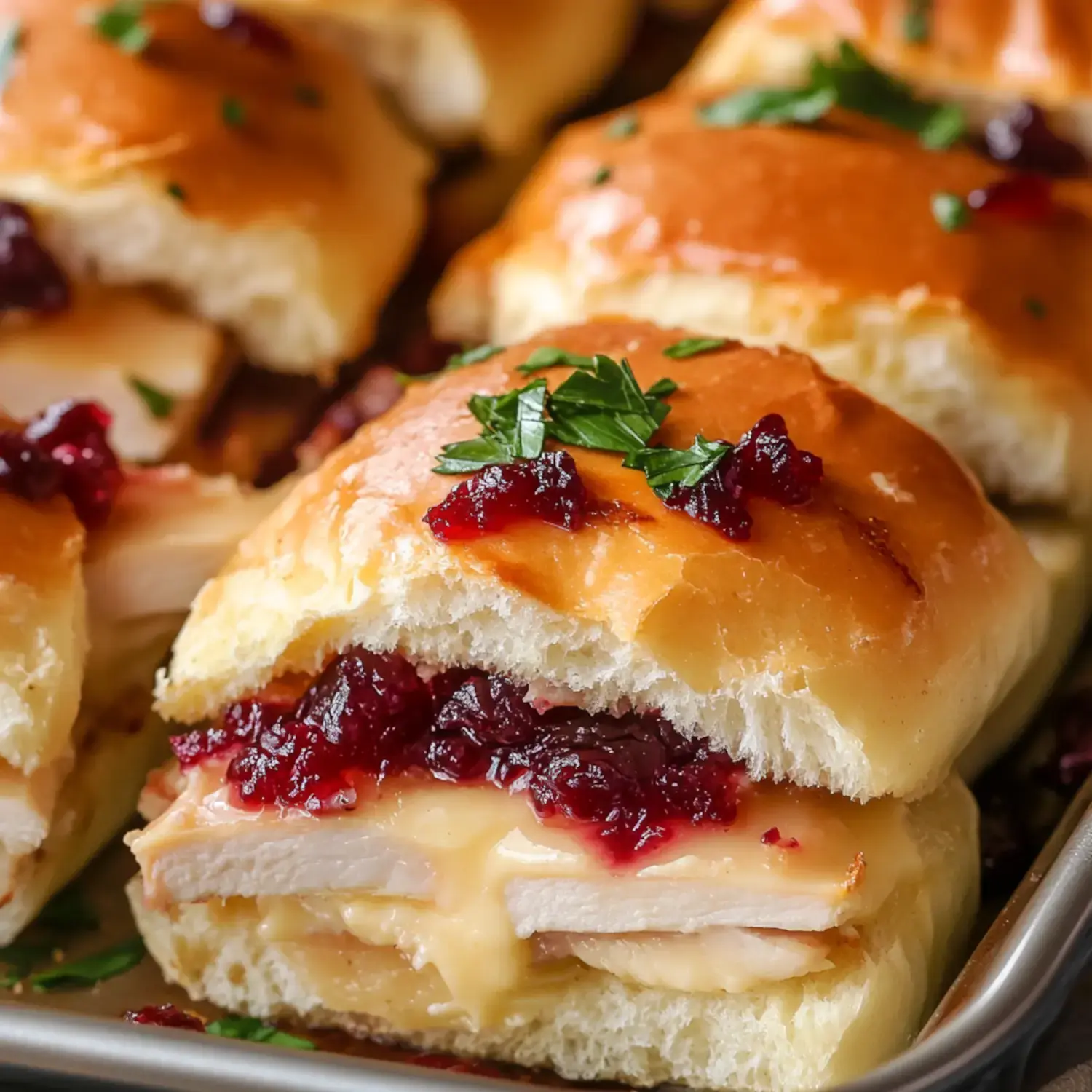 A delicious sandwich on soft bread stuffed with turkey, melted cheese, cranberry sauce, and topped with parsley.