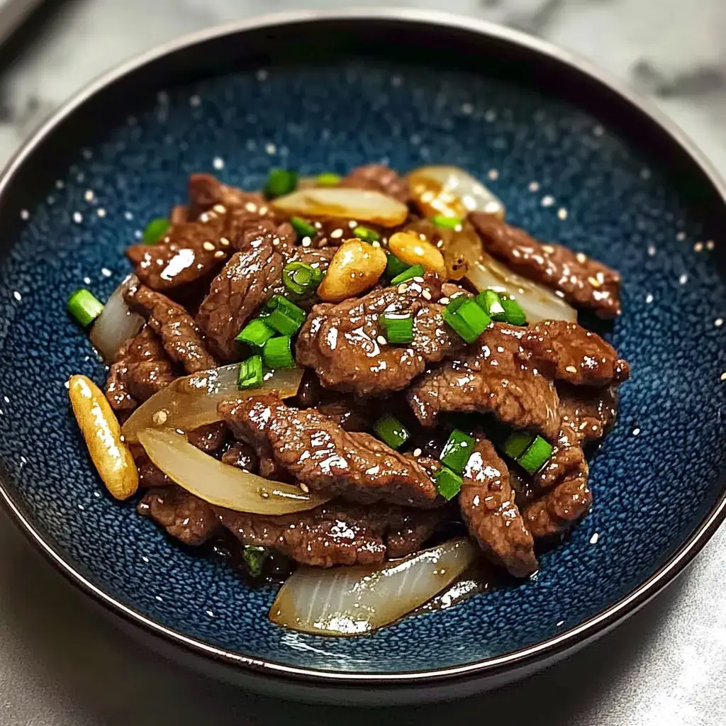 A bowl filled with juicy beef strips, golden onions, topped with green onions, sesame seeds, and nuts for garnish.