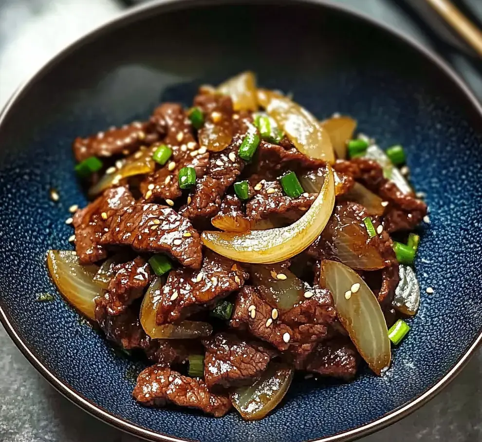 A close-up of a bowl filled with sautéed beef slices, onions, and green onions, garnished with sesame seeds.