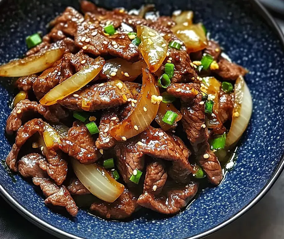 A bowl of stir-fried beef with onions and green onions, garnished with sesame seeds.