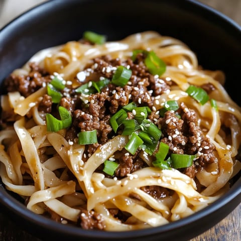 Close-up of stir-fried noodles with ground beef, sesame seeds, and green onions on top.